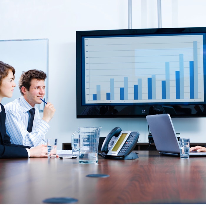 Happy young businesspeople having meeting in boardroom at office in front of a huge plasma TV screen, indoor, smiling.
