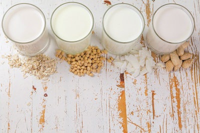 Non-dairy milk alternatives in glasses on white wood background