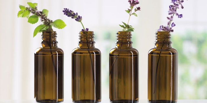 Bottle with essential oil and lily-of-the-valley flowers on color