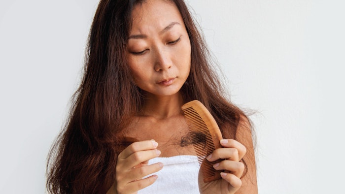 Woman looks at comb with a hair clump inside the bristles.