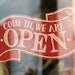 An open sign that reads 'Come in, we are open' hangs on a window front.
