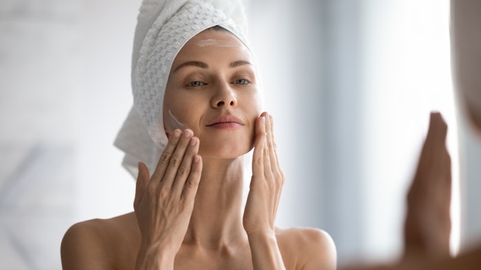 woman using skincare cream in bathroom mirror