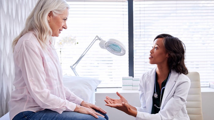 Mature Woman In Consultation With Female Doctor Sitting On Examination Couch In Office