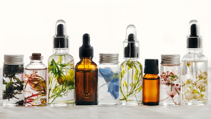 Transparent Bottles of essential oil with fresh herbs.