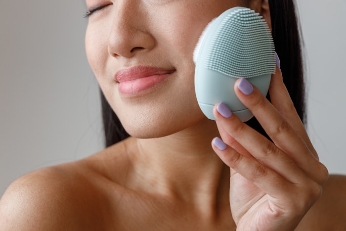 Asian young woman massaging cheek with cleansing massager