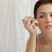 Teen girl with acne problem applying cream near mirror in bathroom