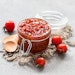 Cherry tomato jam in a glass jar on a linen napkin on a light gray background in rustic style
