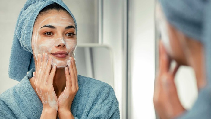Ct2409 Lionetti Hero Image Woman Cleansing Her Face Looking In Mirror Blue Towel Adobe Stock 535197440