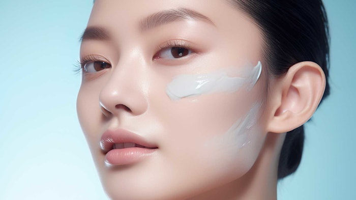 beautiful youthful Asian woman blue background skin cream on her cheek