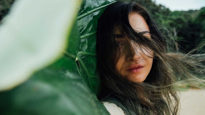 woman outside standing near large leaves wind blowing, beach and jungle background