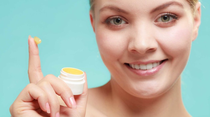 young caucasian woman smiling dipped finger into jar of balm teal bg