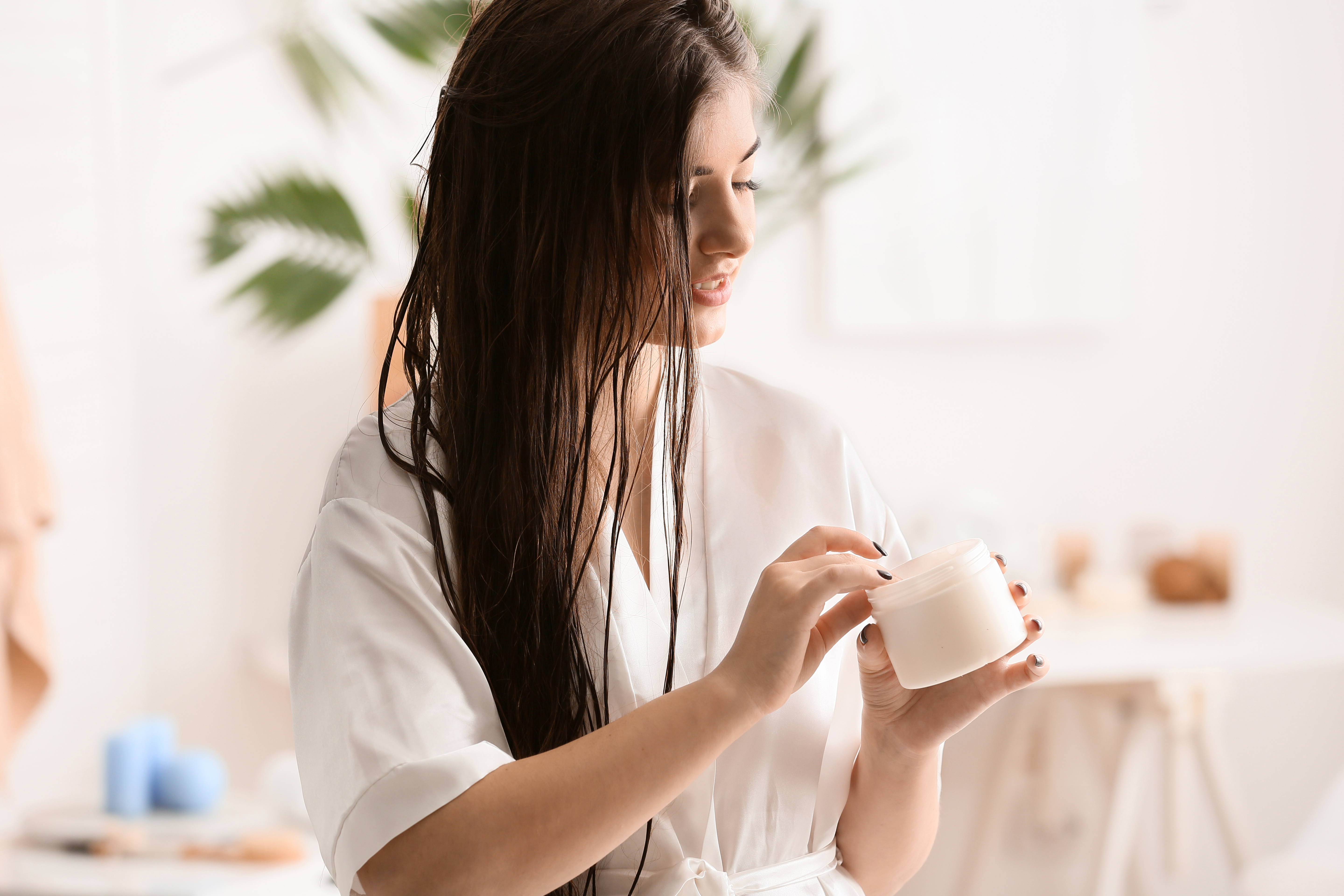 Woman with long brown hair holding a hair mask container.