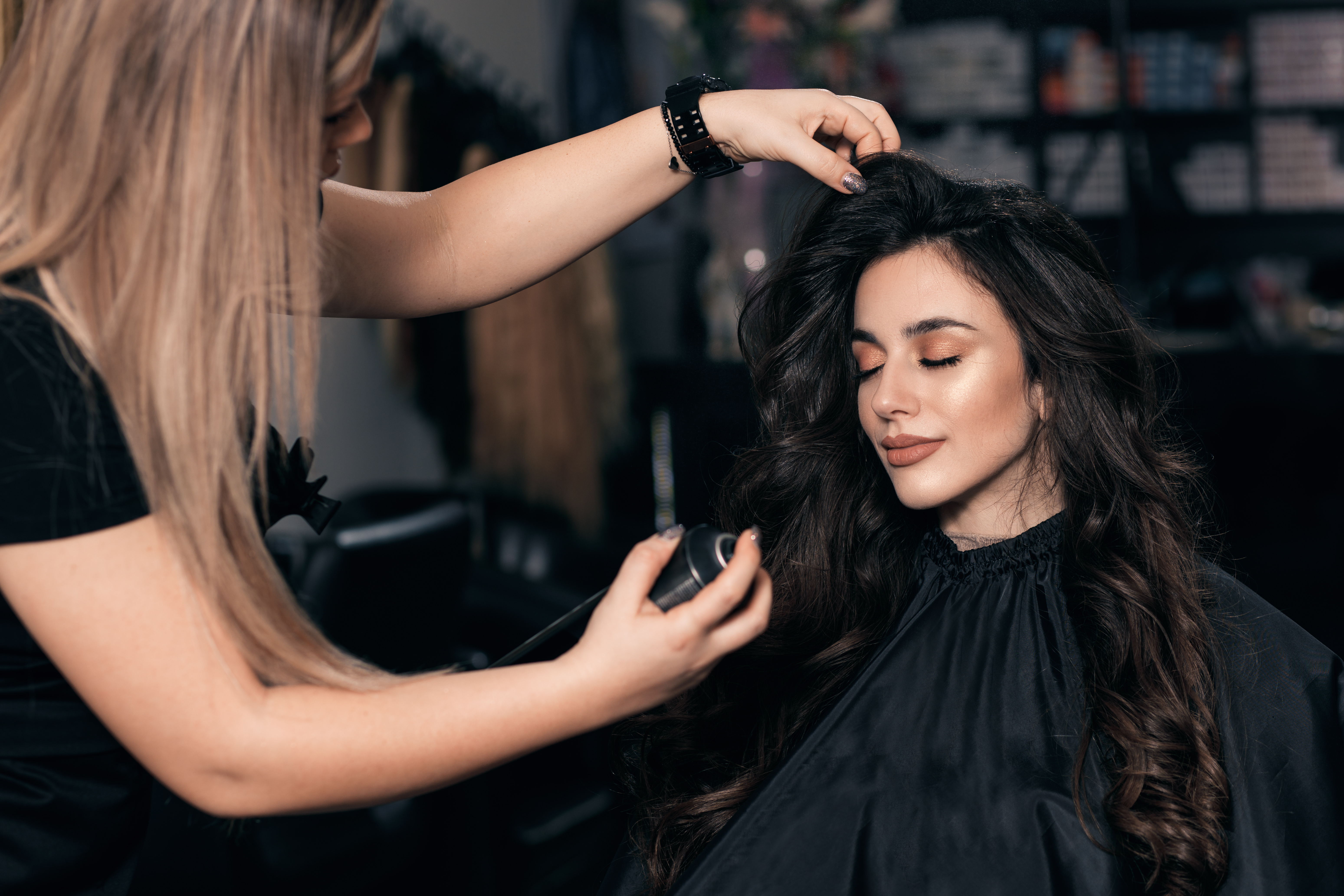 Hair professional styling a client with long, brunette hair by using hair spray.