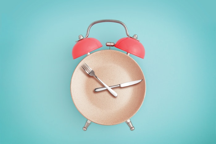 Alarm clock and plate with cutlery. Concept of intermittent fasting, lunchtime, diet and weight loss