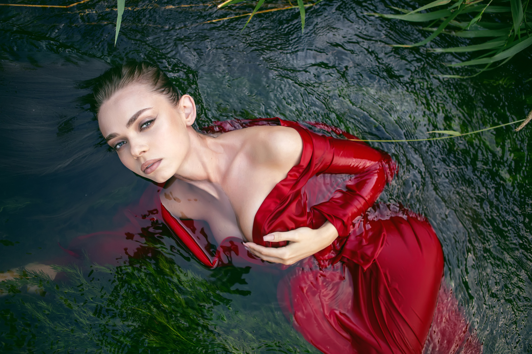 woman in red dress floating in water with algae