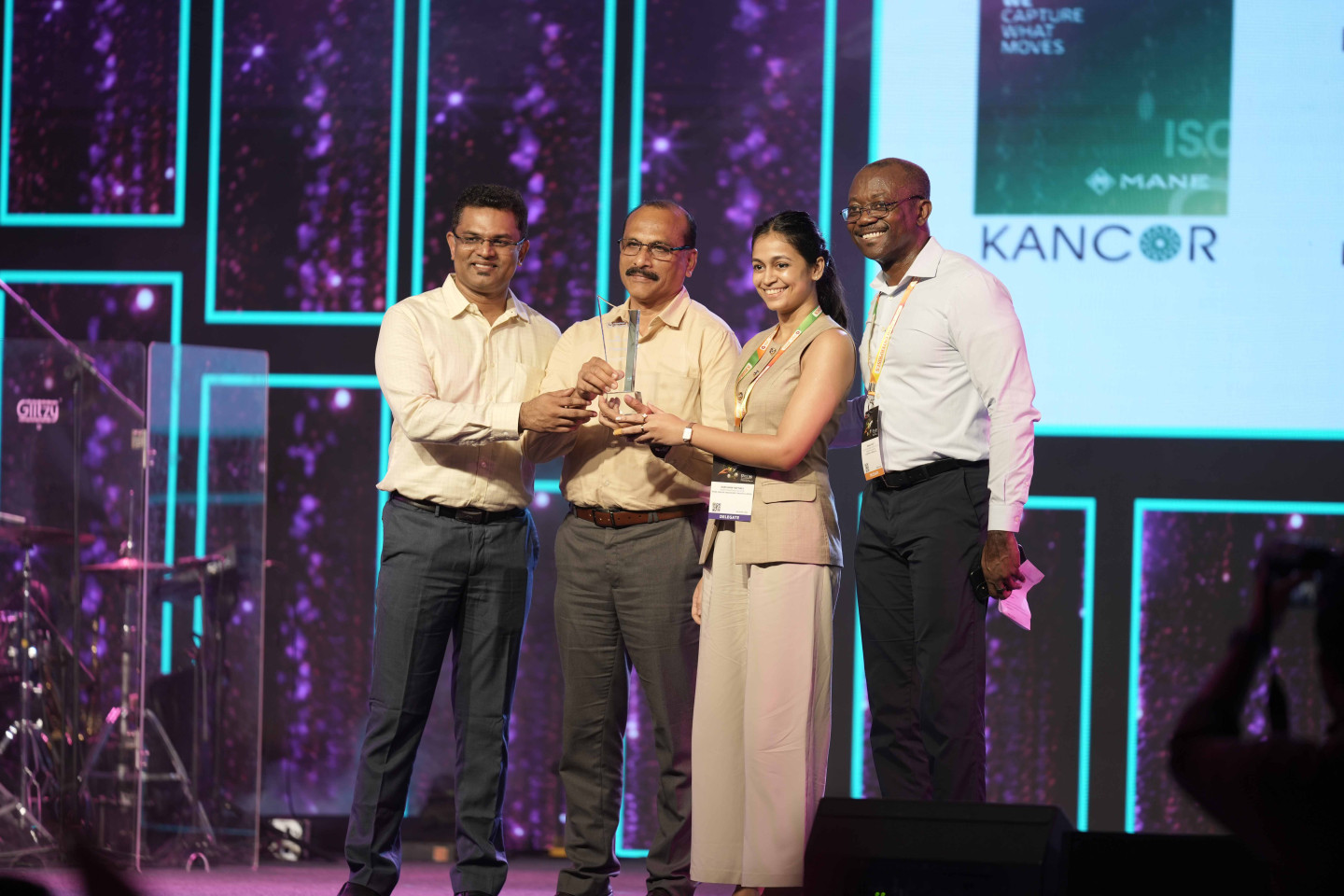 Four professionals on stage at a corporate event holding an award together with purple and cyan stage lighting in background