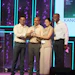 Four professionals on stage at a corporate event holding an award together with purple and cyan stage lighting in background