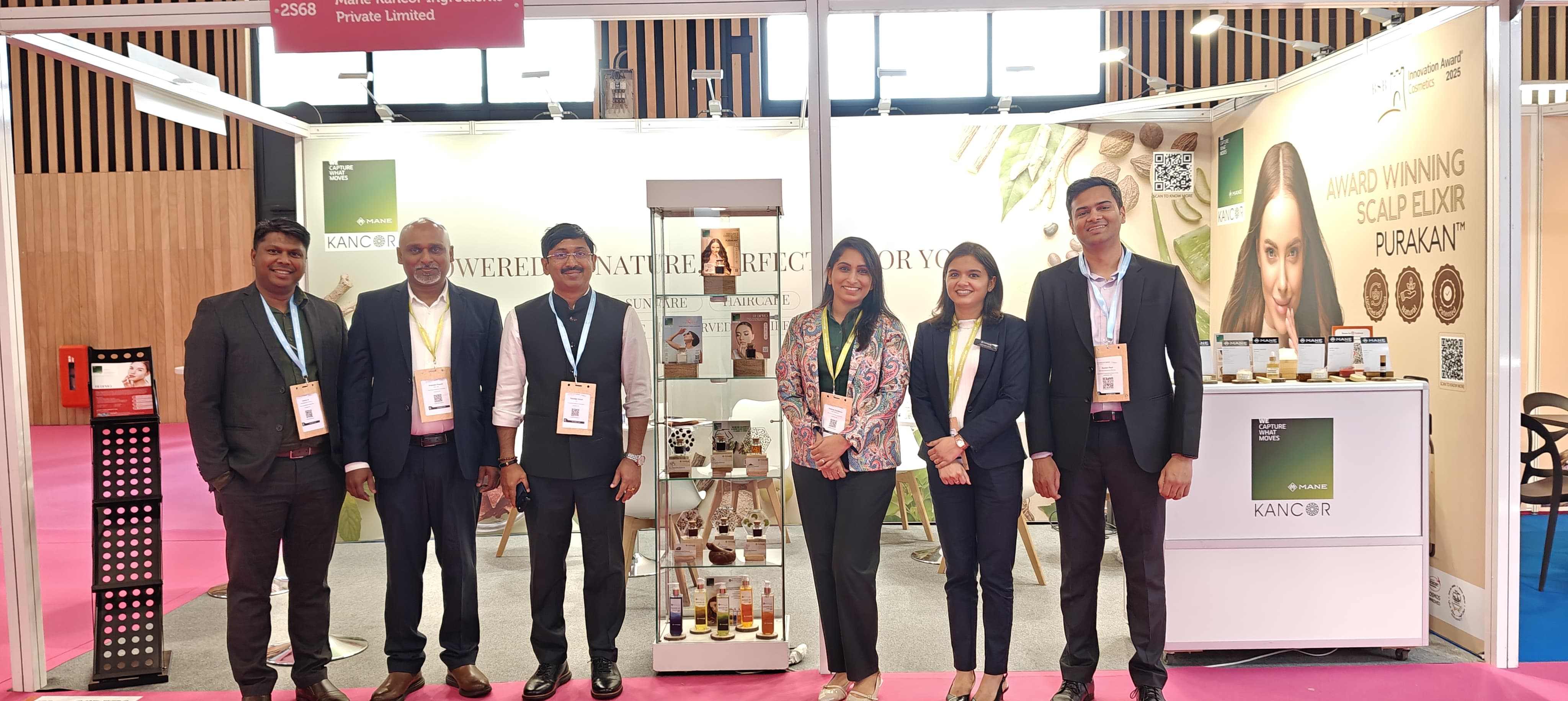 Seven professionals in business attire posing at an exhibition booth with product displays and signage
