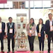 Seven professionals in business attire posing at an exhibition booth with product displays and signage