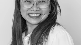 Professional headshot of a smiling woman wearing glasses and a white shirt against a neutral background