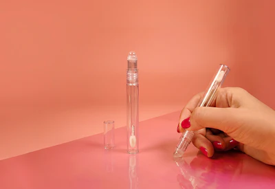 Hand holding clear glass perfume bottle with two additional bottles on coral background