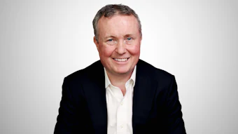 Professional headshot of a smiling man in a dark blazer and white shirt against a light gray background