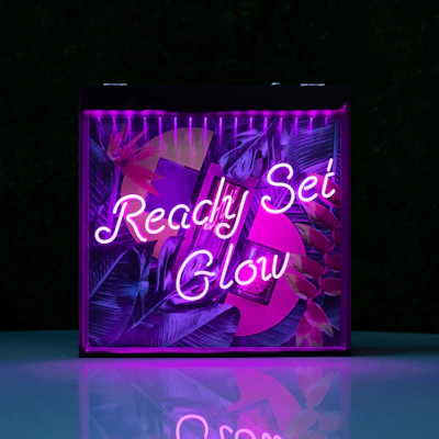 Neon sign reading 'Ready Set Glow' with purple and magenta lighting and tropical leaf graphics