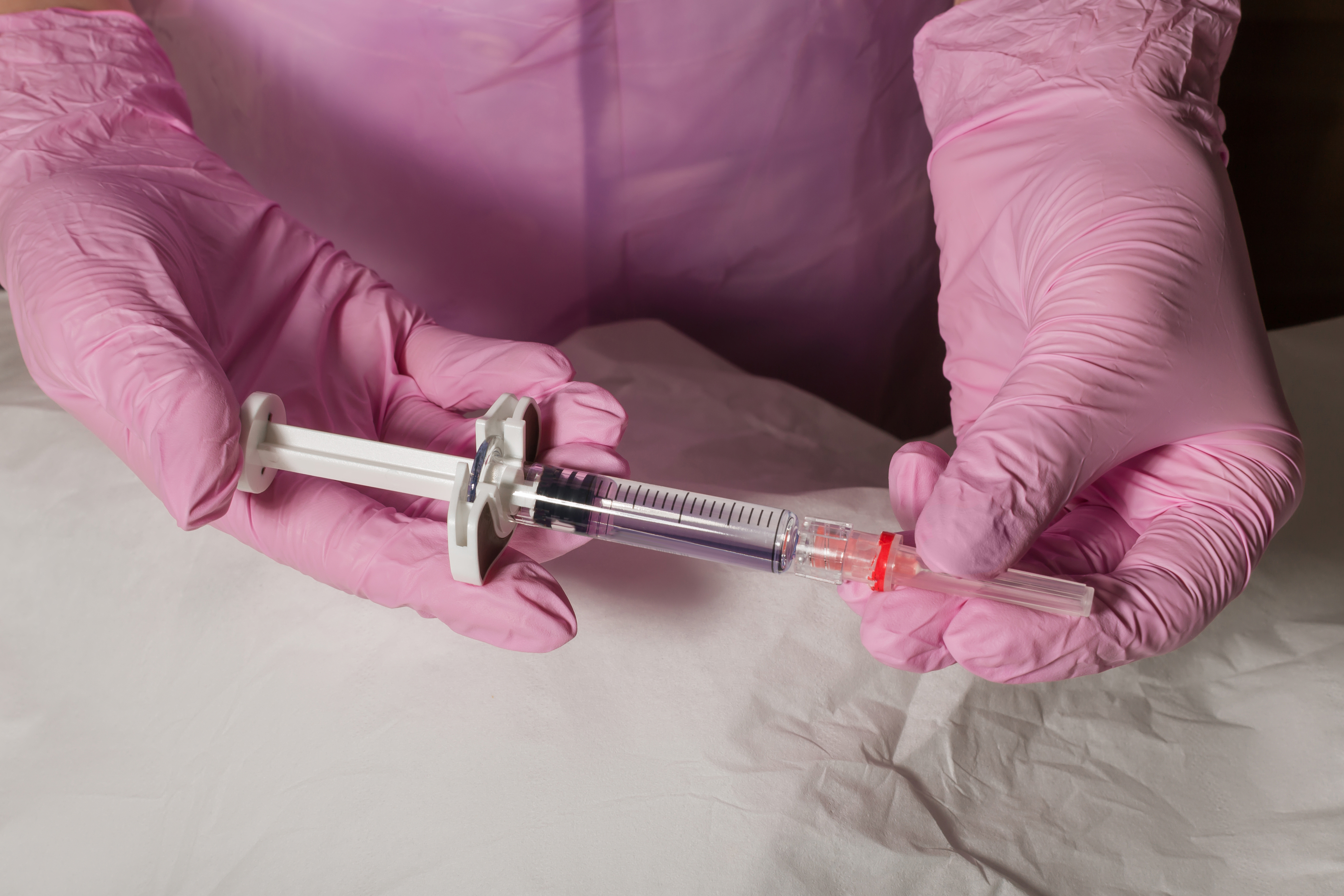 Healthcare professional in pink gloves holding a filled syringe with red cap during medical procedure