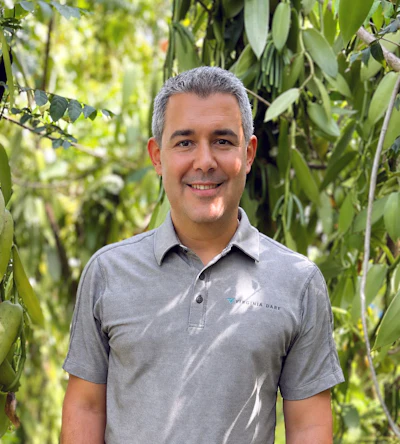 Professional man in gray Virginia Dare polo shirt smiling outdoors surrounded by green foliage