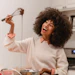 Woman with curly hair laughing while holding a whisk with chocolate batter dripping in a bright kitchen