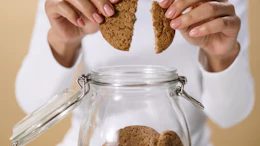 Woman breaking a cookie in half above a glass jar filled with homemade cookies