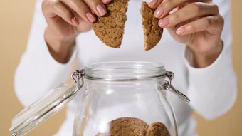 Woman breaking a cookie in half above a glass jar filled with homemade cookies