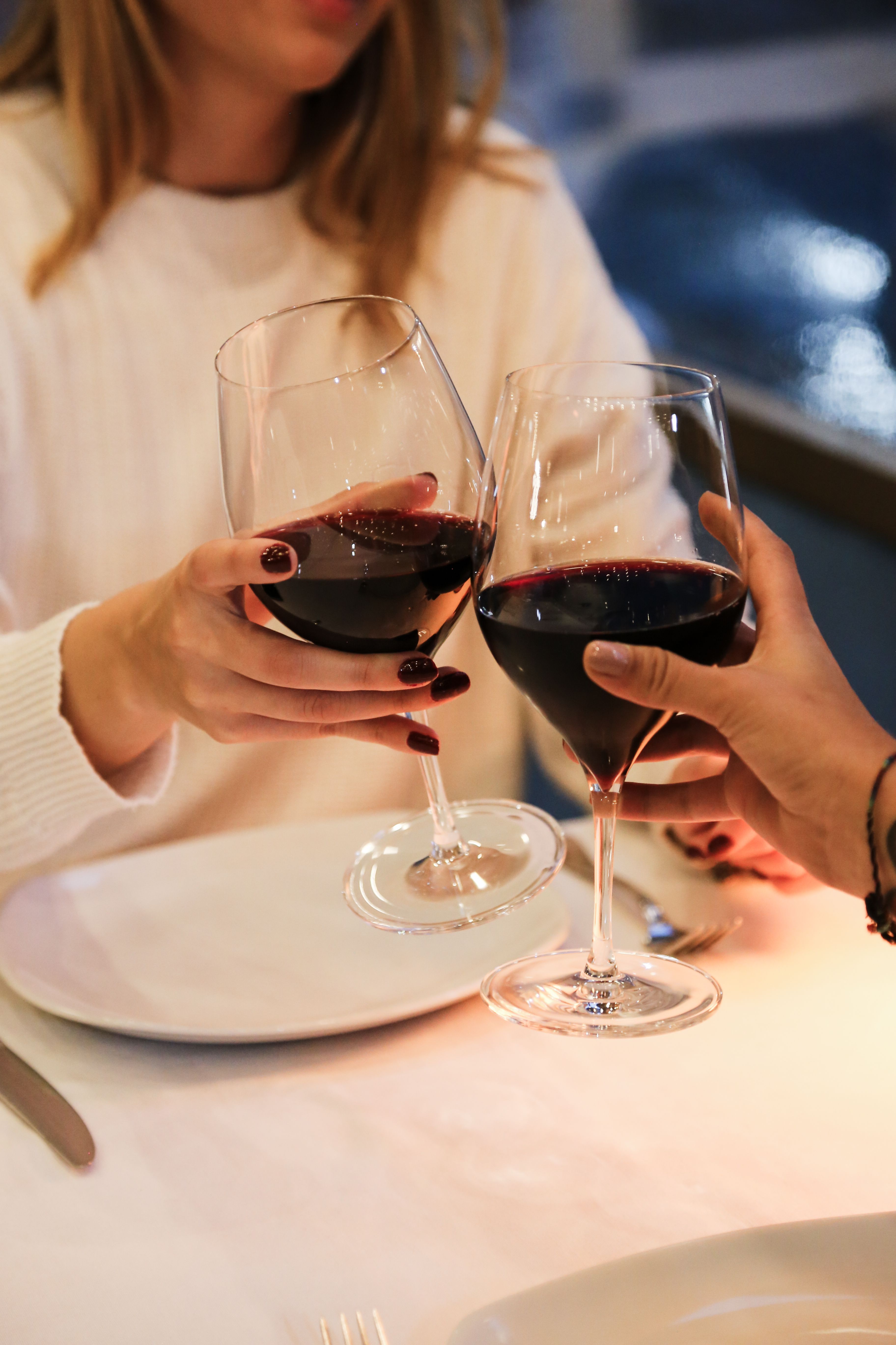 Two people toasting with red wine glasses at a white dining table during an elegant dinner