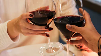 Two people toasting with red wine glasses at a white dining table during an elegant dinner