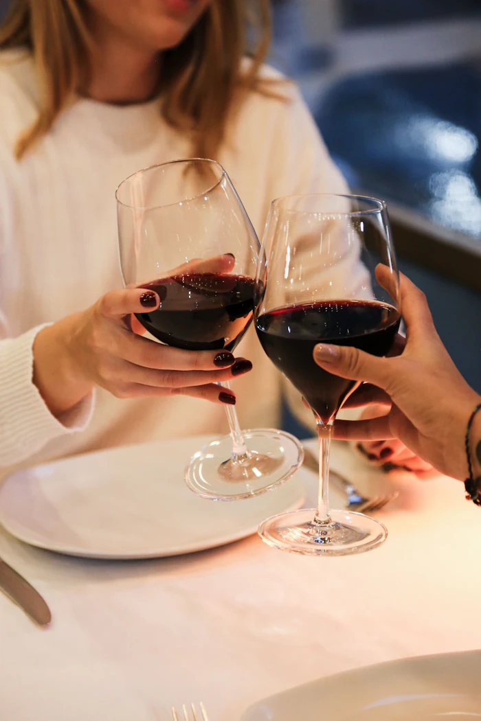 Two people toasting with red wine glasses at a white dining table during an elegant dinner