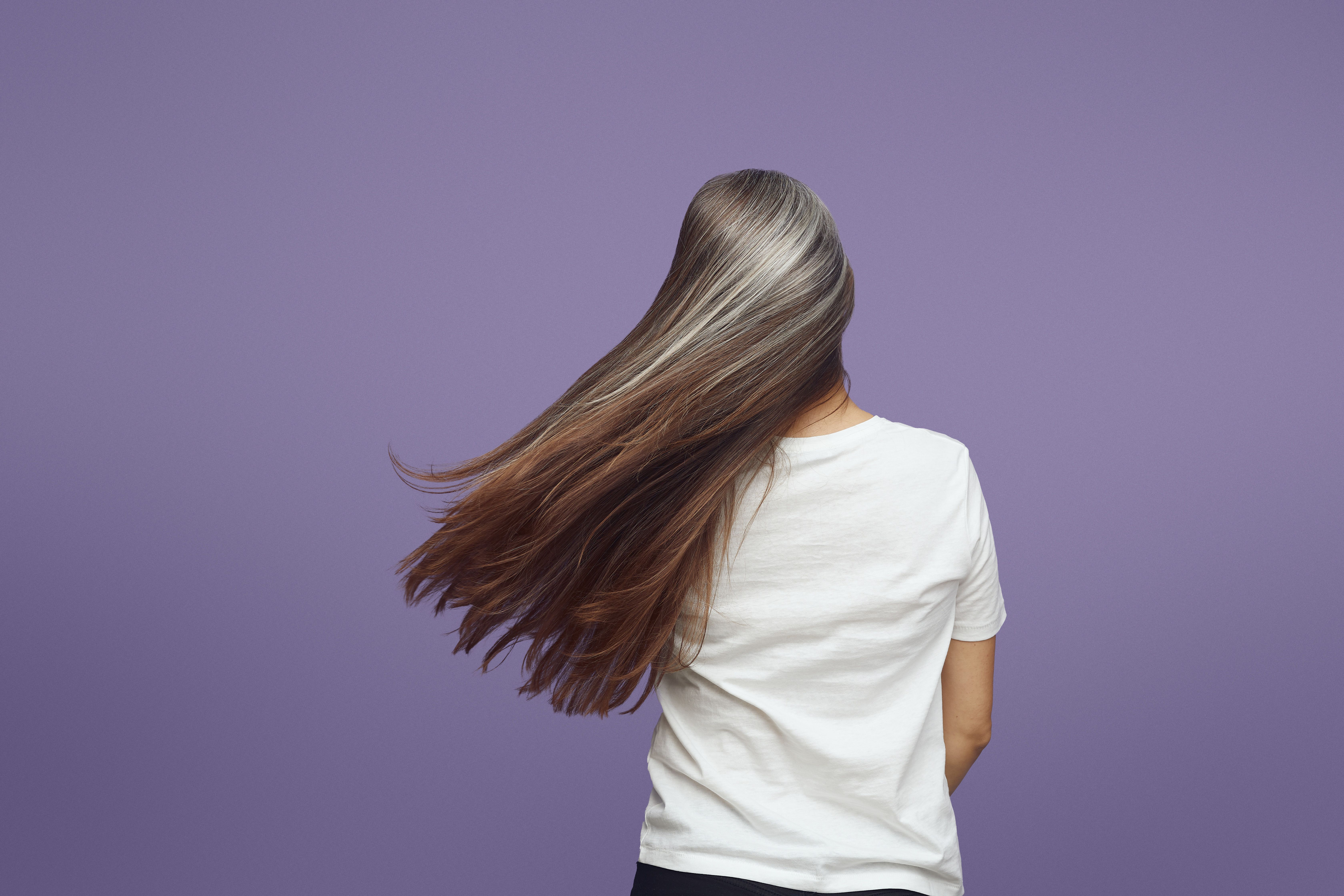 Person with long flowing hair wearing white t-shirt against purple background