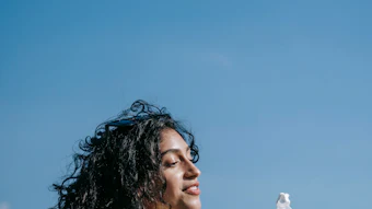 Woman in cream tank top holding beverage bottles outdoors against clear blue sky