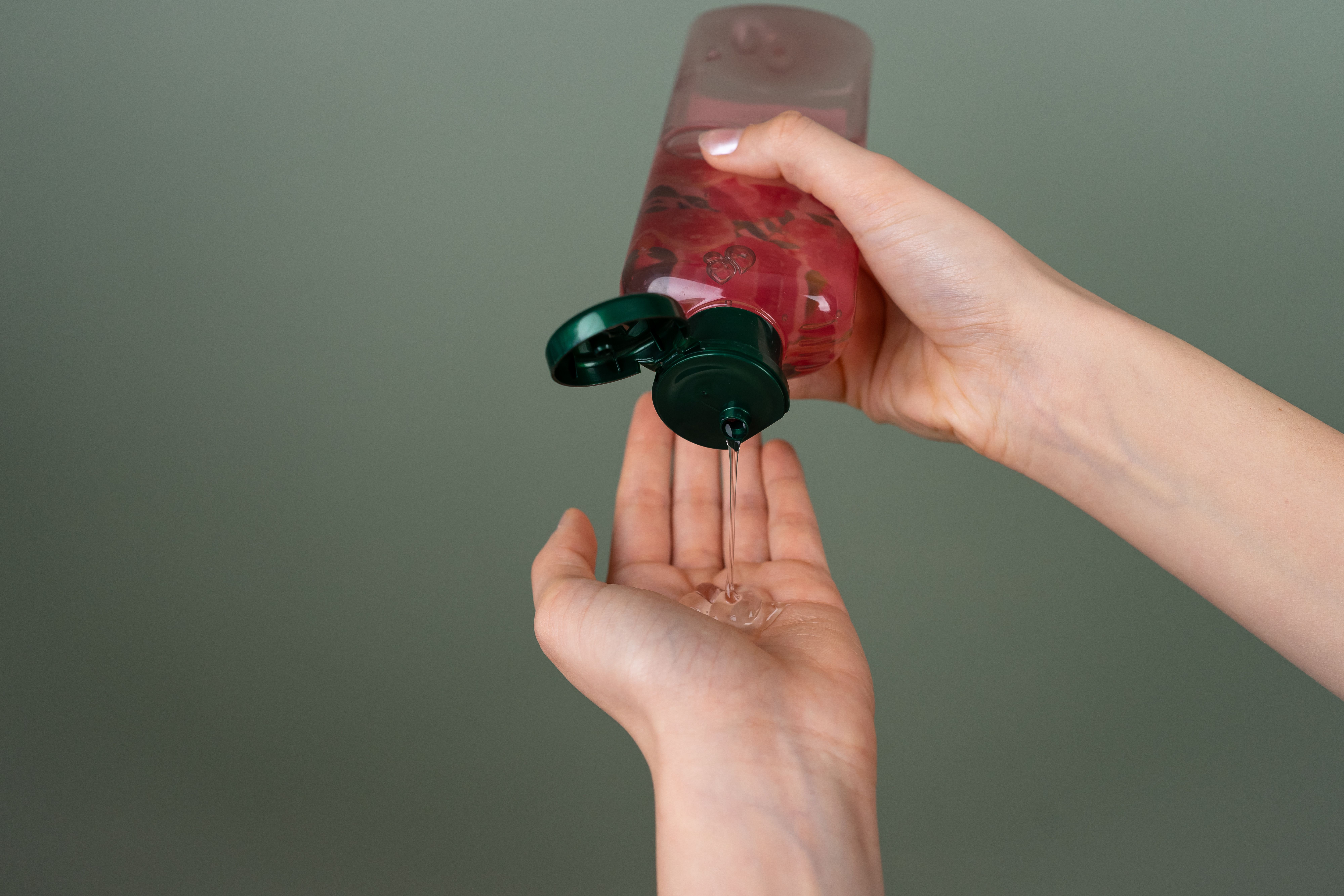 Hands dispensing red liquid from a black pump bottle against green background