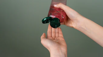 Hands dispensing red liquid from a black pump bottle against green background