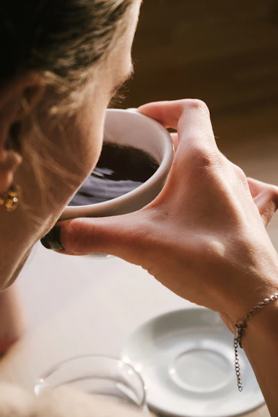 Woman drinking coffee from a white mug with natural sunlight and blurred background