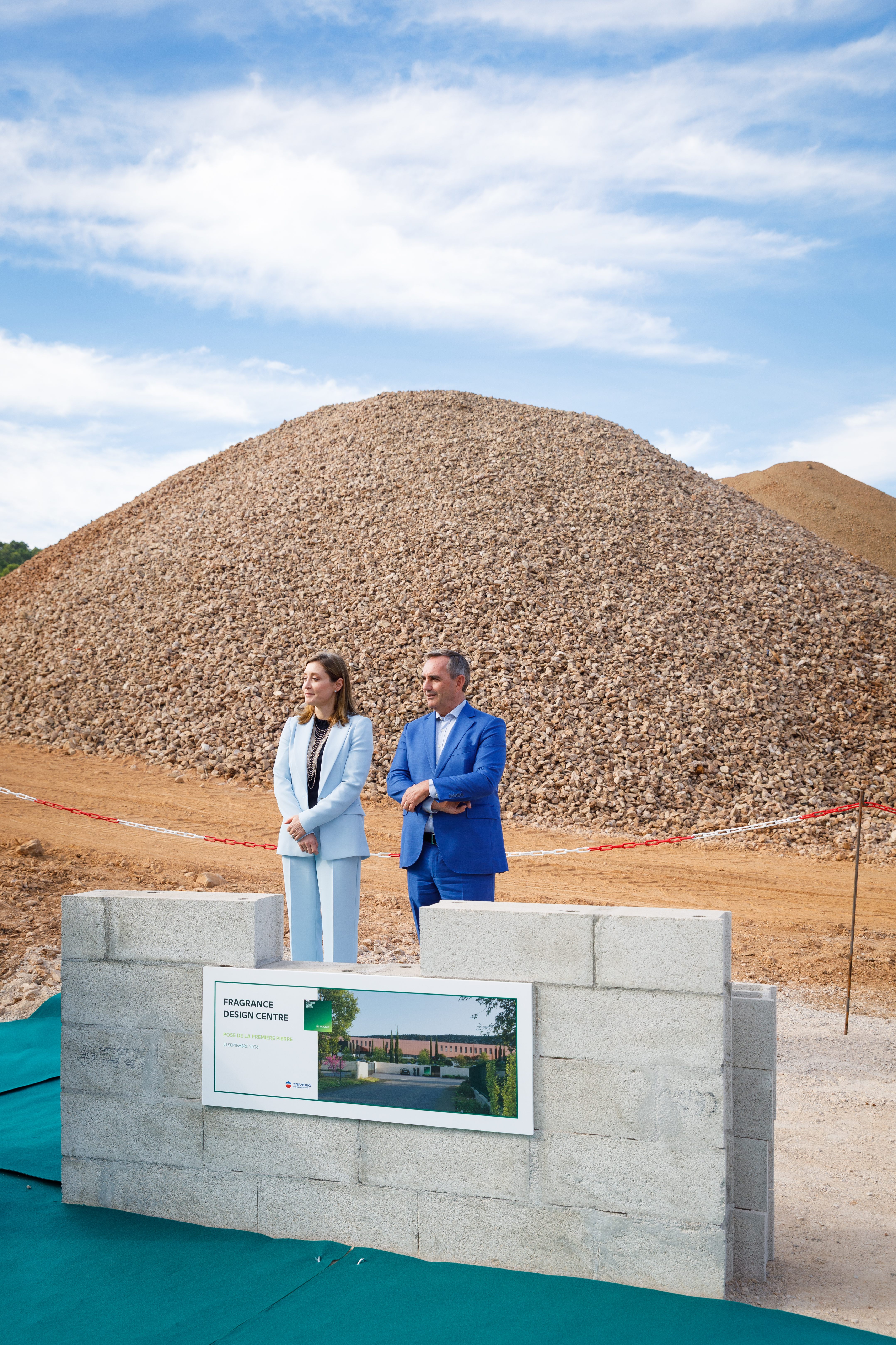 Two professionals stand at construction site with large gravel pile and Fragrance Design Centre signage