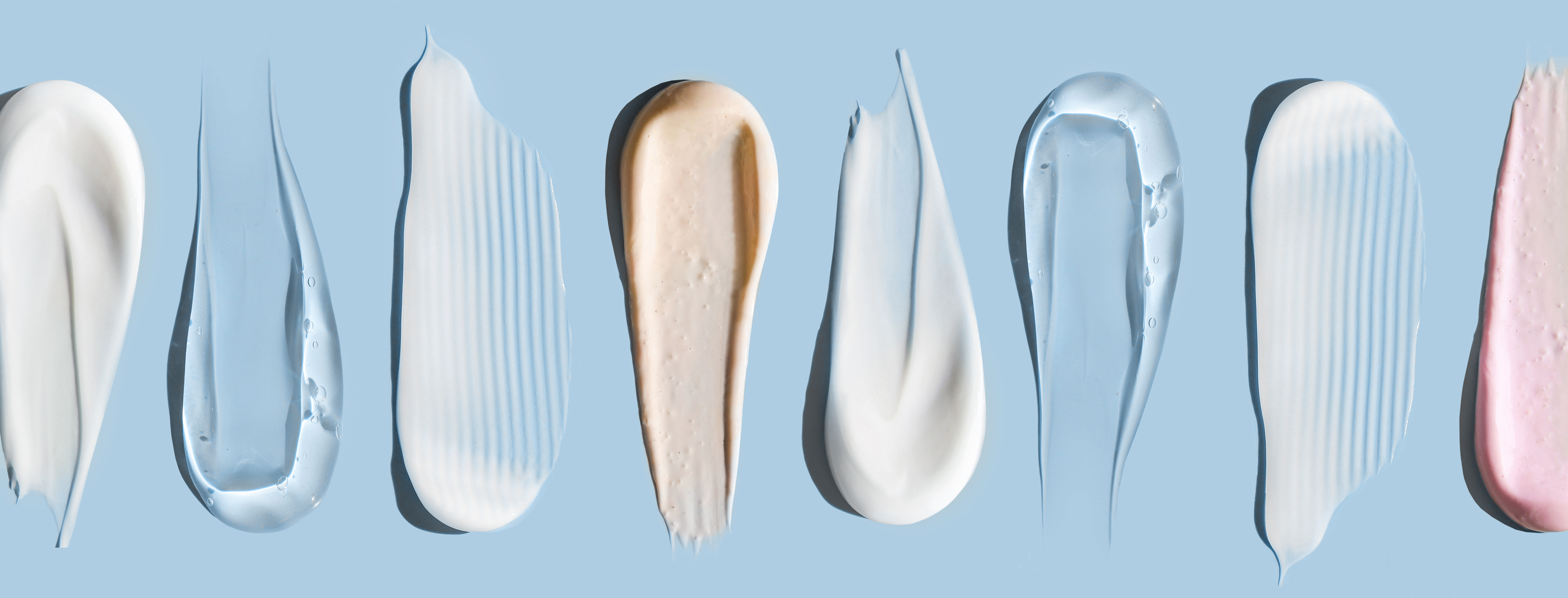 Array of cosmetic and skincare product swatches in white, cream, and pink tones on blue background