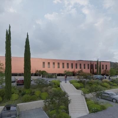 Modern terracotta-colored building with cypress trees, landscaped grounds, parking area, and concrete walkway under cloudy sky