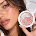 Woman holding open circular makeup palette with swirled red and gold eyeshadow design