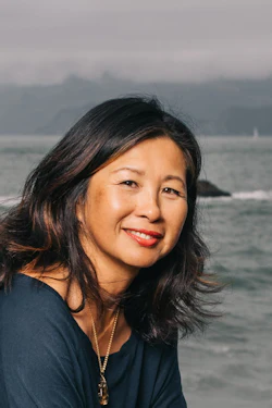 Woman smiling while sitting on rocky outcrop overlooking ocean waves and distant coastline