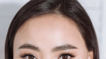 Woman's face partially hidden behind white baby's breath flowers with natural makeup and brown eyes