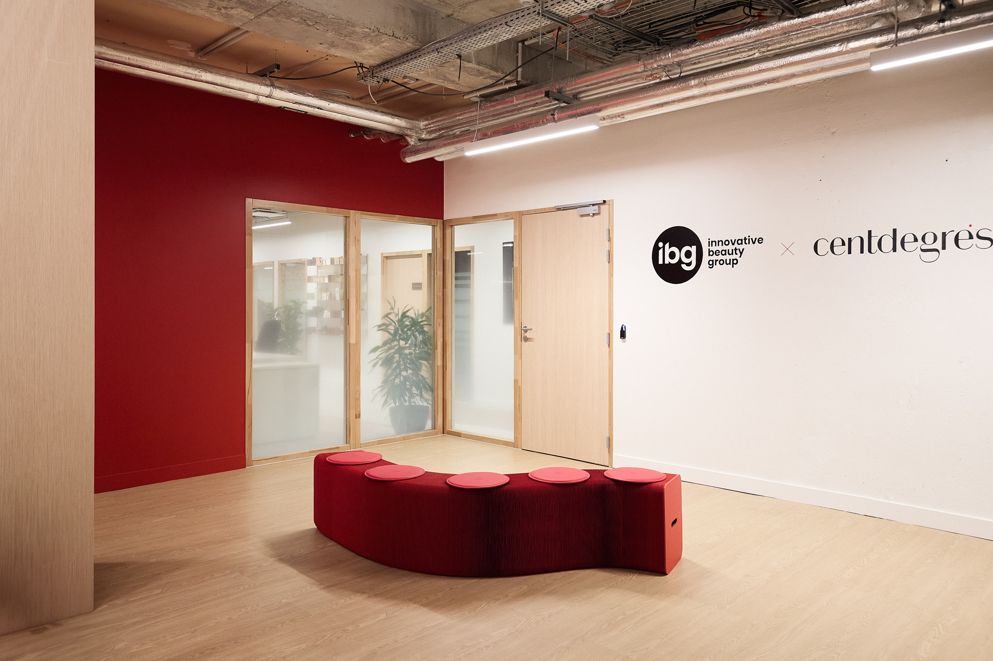 Modern office interior with red curved seating and glass doors, displaying IBG and Centdegres corporate logos on white wall