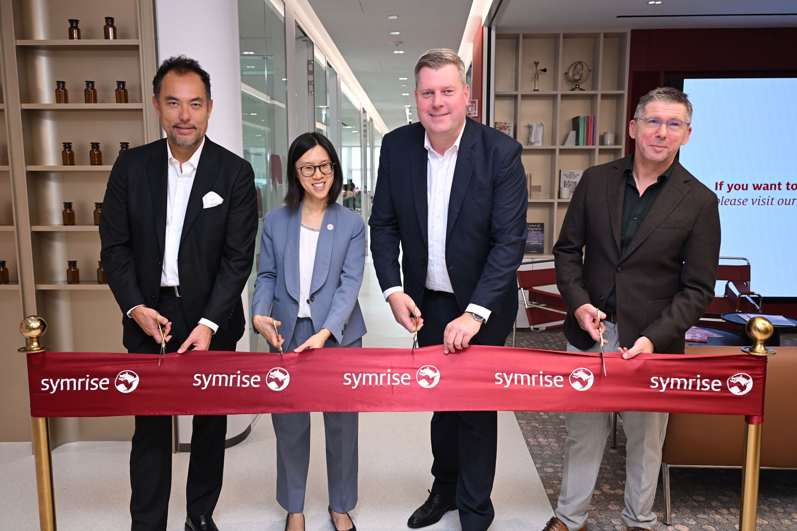 Four professionals at Symrise ribbon-cutting ceremony in modern office with shelving