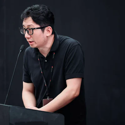 Man wearing glasses speaking at microphone during presentation