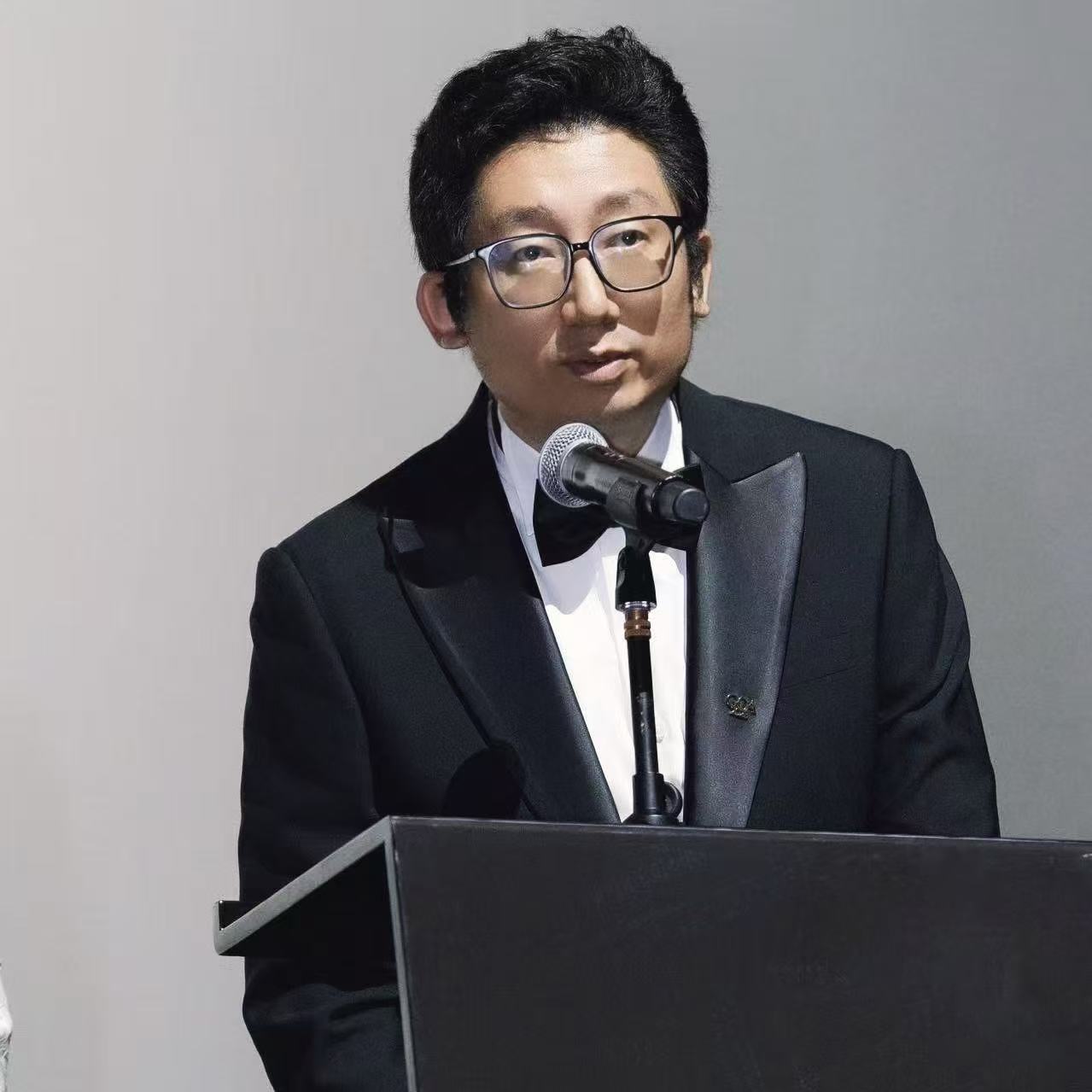 Professional man in glasses and formal attire speaking at podium with microphone during presentation